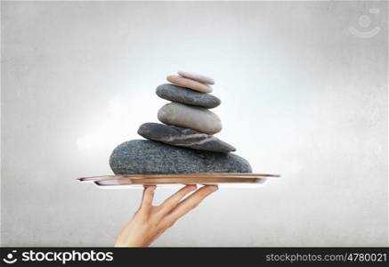 Stones massage procedure. Hand holding metal tray with stack of stones