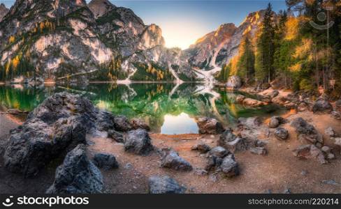 Stones on the coast of Braies lake at sunrise in autumn in Dolomites, Italy. Landscape with mountains, water with reflection, trees in fall. Travel in italian alps. Dolomiti. High rocks and lake
