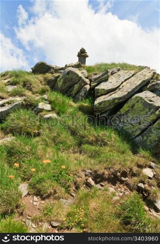 stony post on summer mountain top and yellow flower on slope (Ukraine, Carpathian Mountains)