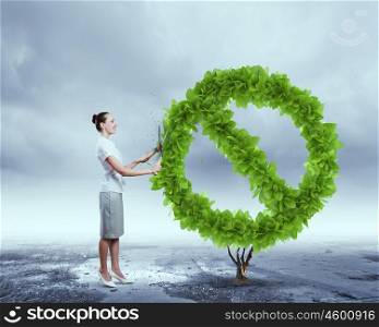 Stop pollution. Young attractive businesswoman cutting plant in shape of prohibition sign