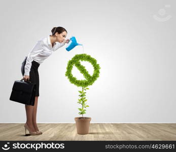 Stop pollution. Young attractive businesswoman watering plant in pot with can