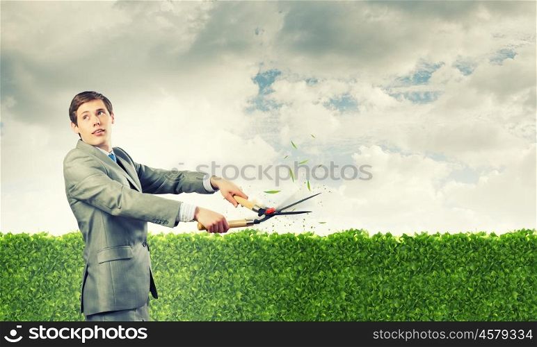 Stop pollution. Young handsome businessman cutting green lawn. Greenery concept