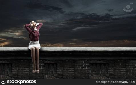 Stop that sound!. Young woman sitting on roof and covering ears with hands