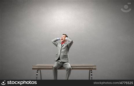Stop this sound. Frustrated businessman on bench closing ears with hands