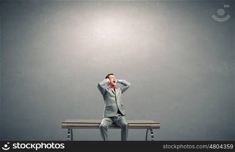Stop this sound. Frustrated businessman on bench closing ears with hands