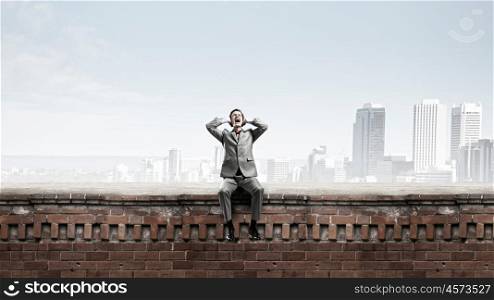 Stop this sound. Frustrated businessman on building top closing ears with hands