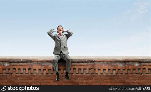 Stop this sound. Frustrated businessman on building top closing ears with hands
