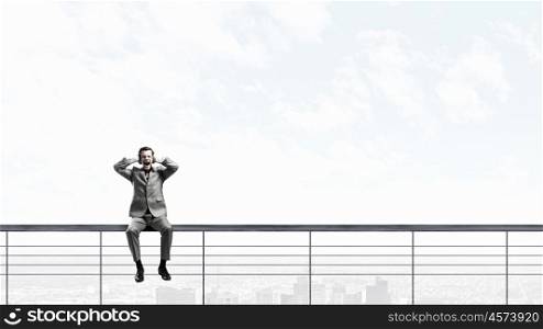 Stop this sound. Frustrated businessman sitting on parapet closing ears with hands