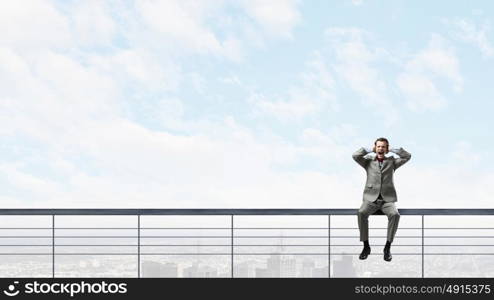 Stop this sound. Frustrated businessman sitting on parapet closing ears with hands