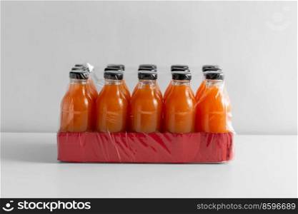 storage, drinks and packaging concept - close up of pack of glass bottles with fruit or vegetable juice on white table. pack of bottles with fruit or vegetable juice