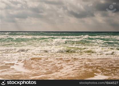 Storm on the sandy beach of the Black Sea coast, emerald clear water, warm day. The sun?s rays make their way through the clouds in the sky.
