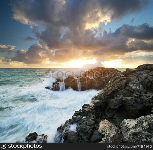 Storm seascape nature composition. Sea waves during storm on sunset splash on stones.