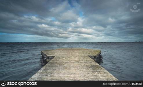 Stormy clouds with dramatic sky above smooth lake made with long exposure photography, Province, Friesland, Holland. Jetty for boats and recreational area for swimmers on the coast of Frisian Lakes