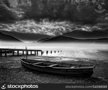 Stormy sky landscape over misty mountain lake with old boat on lake shore