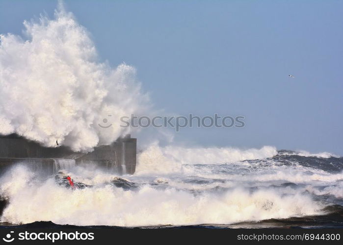 Stormy wave over lighthouse and pier of San Esteban de Pravia in Asturias, Spain.