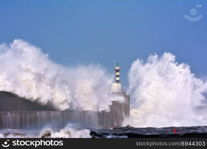 Stormy wave over lighthouse and pier of San Esteban de Pravia in Asturias, Spain.