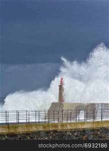 Stormy wave over old lighthouse and pier of Viavelez in Asturias, Spain.