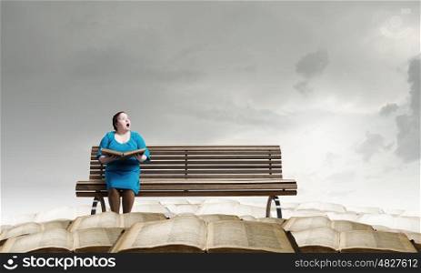 Stout woman. Plus size surprised woman with book in hands sitting on bench
