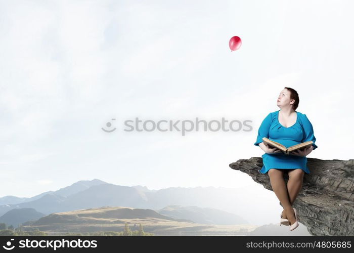 Stout woman. Plus size surprised woman with book in hands sitting on rock edge