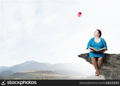 Stout woman. Plus size surprised woman with book in hands sitting on rock edge