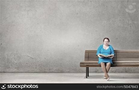 Stout woman. Plus size woman with book in hands sitting on bench