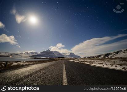 straight country road under the moonlight with dramatic clouds and starry sky, Iceland