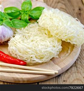 Stranded rice noodles with garlic, red pepper, ginger and basil, chopsticks on a wooden boards background