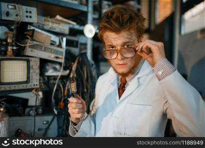 Strange engineer holds electric tube in laboratory. Electrical testing tools on background. Lab equipment, engineering workshop