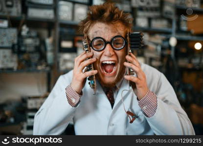 Strange engineer holds electronic chips at his face in laboratory. Electrical testing tools on background. Lab equipment, engineering workshop