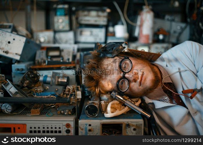 Strange engineer sleeping on devices in laboratory. Electrical testing tools on background. Lab equipment, engineering workshop. Strange engineer sleeping on devices in lab