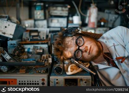 Strange engineer sleeping on devices in laboratory. Electrical testing tools on background. Lab equipment, engineering workshop. Strange engineer sleeping on devices in lab