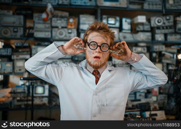 Strange engineer with electric lamps in his ears, test in laboratory. Electrical testing tools on background. Lab equipment, engineering workshop
