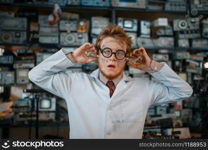 Strange engineer with electric lamps in his ears, test in laboratory. Electrical testing tools on background. Lab equipment, engineering workshop