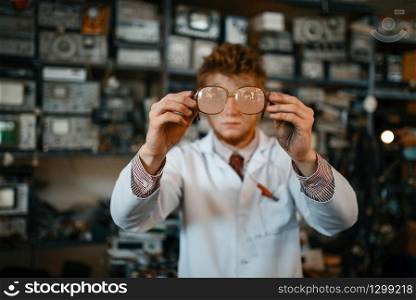 Strange scientist looks through the glasses in laboratory. Electrical testing tools on background. Lab equipment, engineering workshop