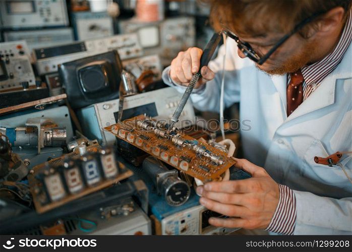 Strange scientist soldering chips, test in laboratory. Electrical testing tools on background. Lab equipment, engineering workshop