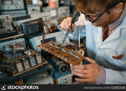Strange scientist soldering chips, test in laboratory. Electrical testing tools on background. Lab equipment, engineering workshop