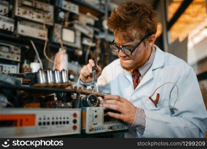 Strange scientist soldering chips, test in laboratory. Electrical testing tools on background. Lab equipment, engineering workshop. Strange scientist soldering chips, test in lab