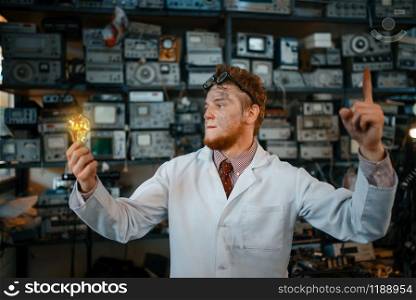 Strange scientist with a burning light in his hands, test in laboratory. Electrical testing tools on background. Lab equipment, engineering workshop