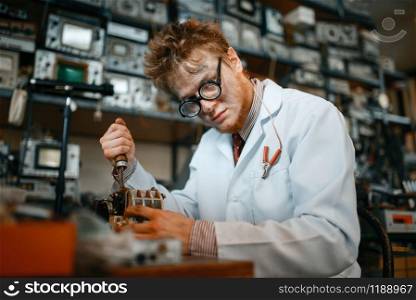 Strange scientist works with soldering iron, test in laboratory. Electrical testing tools on background. Lab equipment, engineering workshop. Strange scientist works with soldering iron in lab