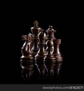 Strategy and leadership concept; black wooden chess figures standing together as a family ready for game against dark background.