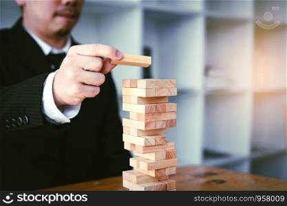 Strategy concept and hand of businessman playing wood blocks stacks game with planning.