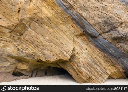 Stratiform rock on sandy beach with small cavern.
