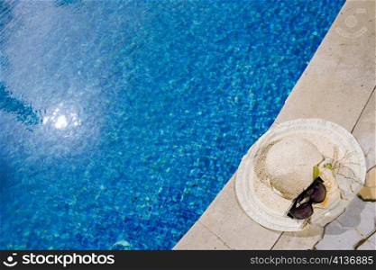 Straw hat and Sunglasses lies on the brink of pool