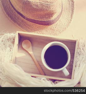 Straw hat with black coffee and spoon on wooden tray, retro filter effect