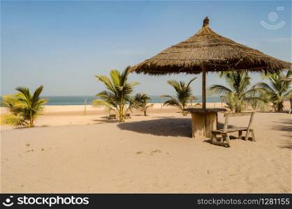 Straw umbrella with a small wooden bench and a table on Bijilo Beach in The Gambia
