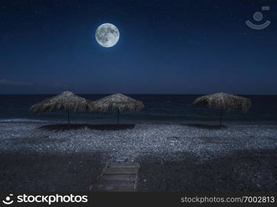 Straw umbrellas on the beach in the night. Moonlight on sea. Night starry sky. 