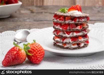 Strawberries desert with cream and wafer served on plate over table top.