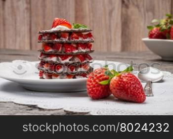 Strawberries desert with cream and wafer served on plate over table top.