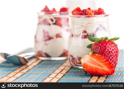 Strawberries desert with cream served on glass cups over table top.