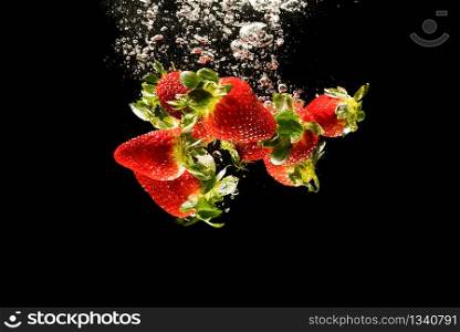 Strawberries falling into water causing bubbles all around it. Healthy food concept. Black background. Strawberries falling into water causing bubbles all around it. Healthy food concept